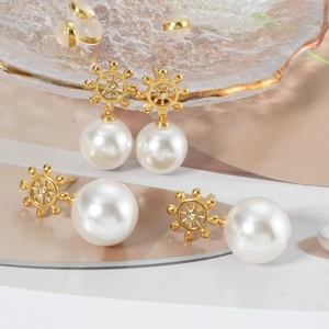 Detail of 18k gold plated nautical helm earrings with pearl drops and silicone backings
