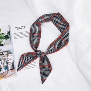 Detail of red and black plaid silk scarf tied in a bow on a white fabric background