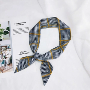 Detail of an orange plaid skinny scarf tied in a knot on a white fabric background