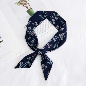 Detail of navy blue floral skinny silk scarf tied in a bow on a lifestyle background
