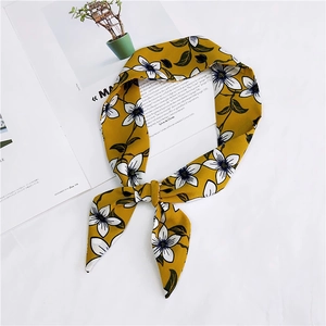 Detail view of a yellow floral chiffon skinny scarf tied over a magazine on white desk