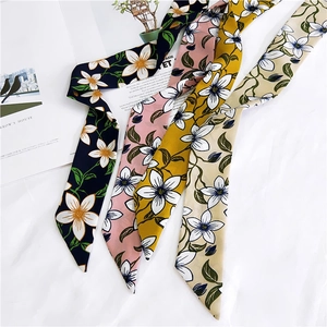 Detailed view of long floral silk scarves in navy pink yellow and beige displayed on fabric