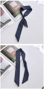 Detail of navy blue polka dot skinny silk scarf styled as a knot on a white desk
