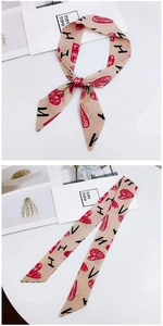 Detail of a beige twilly silk scarf with red hearts and H pattern on a white table