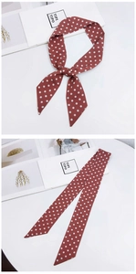 Detail of red and white polka dot silk skinny scarf tied and laid flat on a table