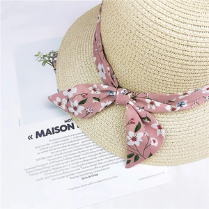 Elegant beige straw sun hat featuring a pink floral ribbon bow on a fashion magazine