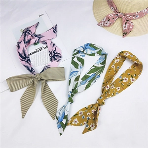 Three long floral silk scarves in pink, blue, and yellow tied as bows for hair or bags