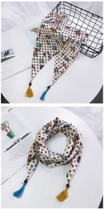 Détail d'un foulard en soie imprimé avec motif paisley, perles en bois et pompons colorés