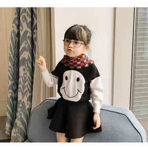 Close-up of kids black and white smiley knit sweater with red plaid scarf on a sofa