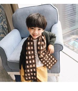 Close-up of thick plaid knit scarf for kids in brown and beige tones on a cozy background