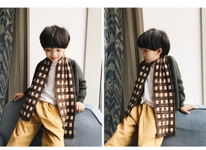 Detail of child wearing a thick brown and beige checkered knit scarf for autumn and winter