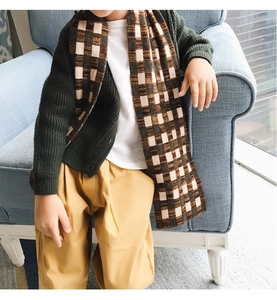 Detailed view of child wearing thick plaid knit scarf with dark green cardigan sweater