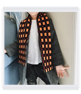 Detail of child wearing a long thick orange and black checkerboard knit scarf