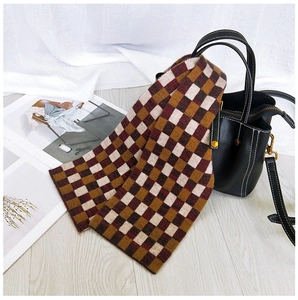 Close-up of a thick checkered knit scarf in red and brown draped over a leather bag