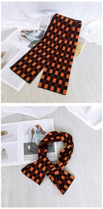 Close-up of thick knitted checkered scarf in orange, dark red, and black patterns