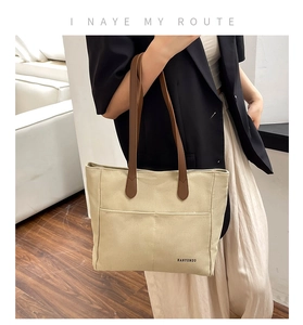 Detail of beige canvas tote bag with brown straps and exterior front pockets