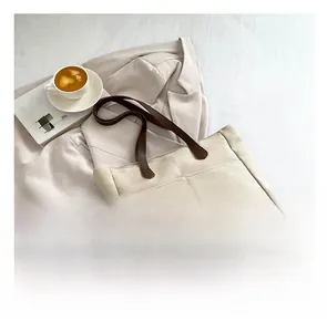 Detail of a large cream canvas tote bag with brown leather straps and front pocket