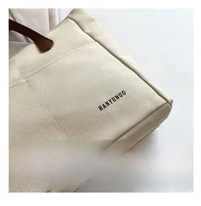 Detail of off-white canvas tote with black HANYUNUO lettering and brown leather handle