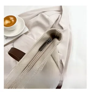 Detail shot of a large canvas tote bag with smooth metal zipper and brown leather straps