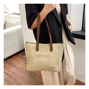 Detail of beige canvas tote bag with dual exterior pockets and brown leather straps