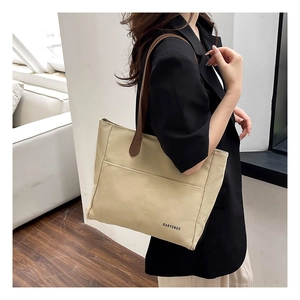 Close-up of beige canvas tote bag featuring brown leather shoulder straps and outer pockets