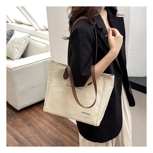 Detail of off-white canvas tote bag with brown leather straps shown on shoulder
