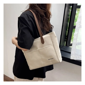 Detail of canvas tote bag featuring brown faux leather straps and a front pocket