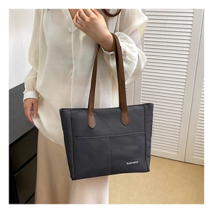 Detail of grey canvas tote bag featuring dual front pockets and brown shoulder straps