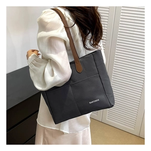 Detail of dark grey canvas tote with brown leather handles worn by a person