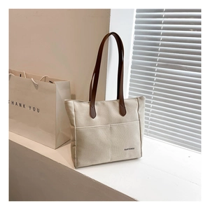 Detail of beige canvas tote with brown handles and exterior pocket on a white background