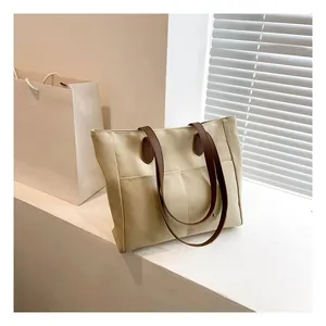 Detail view of a beige canvas tote bag with brown leather handles and two front pockets