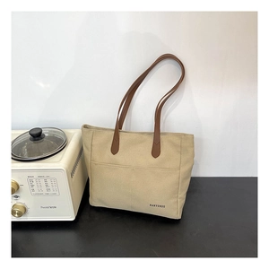 Detail of beige canvas tote bag showing partitioned outer pockets and brown leather handles