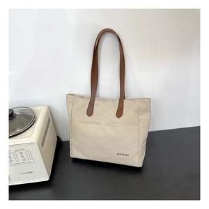 Close-up of beige canvas tote bag with brown leather handles and brand logo detail