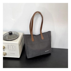 Detail view of large gray canvas tote bag with brown leather handles on a table