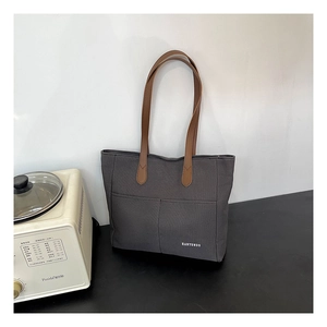 Detail of dark grey canvas tote bag with brown faux leather straps and brand logo