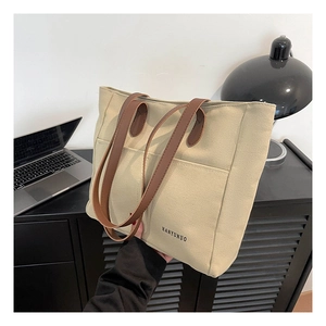Close-up of cream canvas tote bag with brown leather handles and brand logo detail
