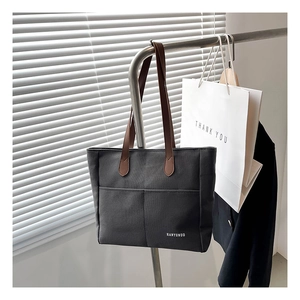 Detail view of black canvas tote bag with brown leather handles and a front pocket