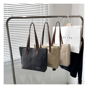 Detailed display of large canvas tote bags in black, khaki, and cream hanging on a rack