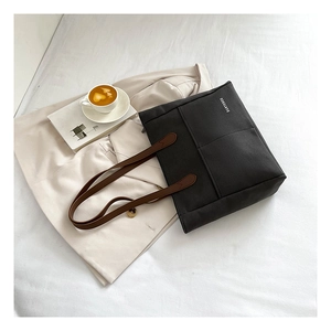 Detail of a black canvas tote with brown leather straps on a beige blazer background