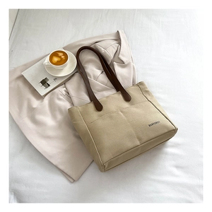 Detail of a beige canvas tote bag with brown leather handles on a lifestyle setting