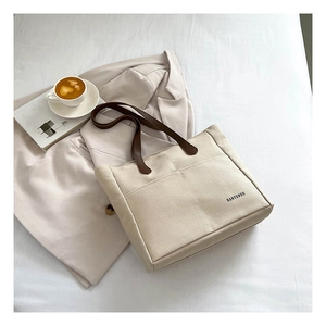 Detail view of cream canvas tote bag with brown leather straps and front layered pockets