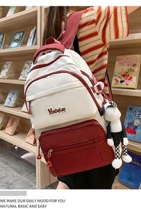 Détail d'un sac à dos scolaire rouge et blanc avec breloque mouton devant une bibliothèque