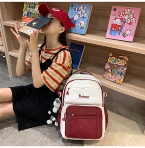 Détail d'un sac à dos en toile rouge et blanc avec poche filet et breloque poupée