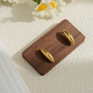 Minimalist golden bean stud earrings in polished stainless steel on a wooden stand