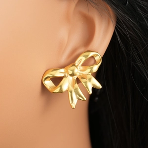 Polished 18k gold plated stainless steel bow earrings worn by a model in a close-up view
