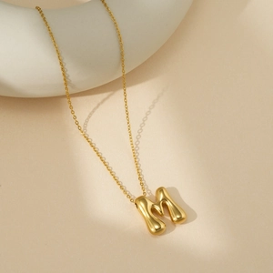 Vue rapprochée du pendentif lettre M en or 18K poli sur un support au design minimaliste