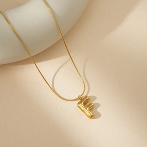 Detalle macro del colgante letra F burbuja en oro 18K con una fina cadena de serpiente