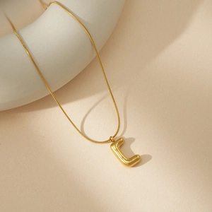 Detalle de un collar con colgante de letra C dorada en 3D sobre soporte minimalista