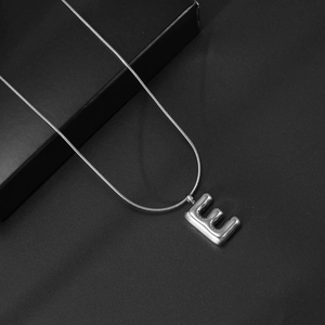 Detail van de 3D zilveren letter E hanger aan een gladde metalen slangenketting ketting