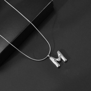 Detailopname van de gepolijste letter M hanger aan een slanke zilveren slangenketting